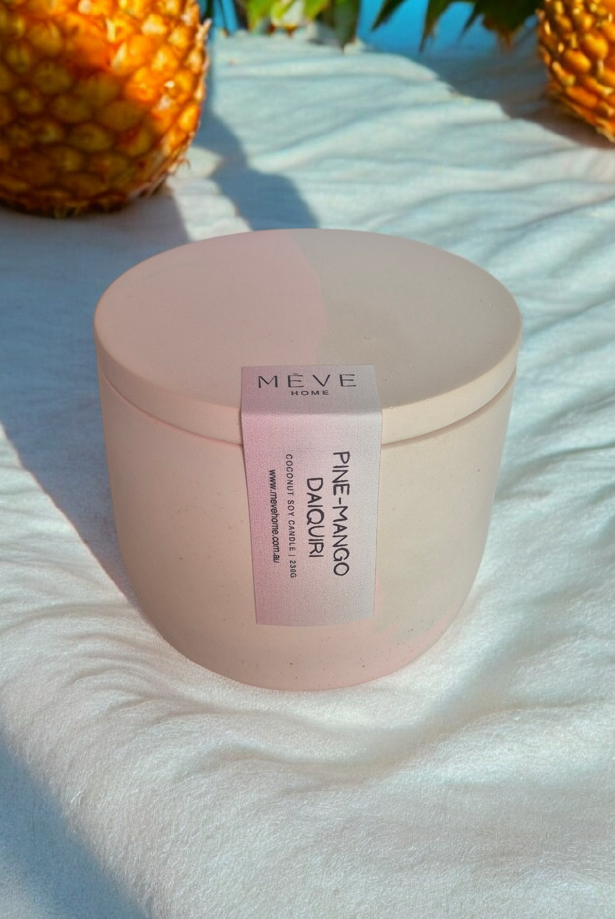 Pink container with a label on a white surface with pineapples in the background