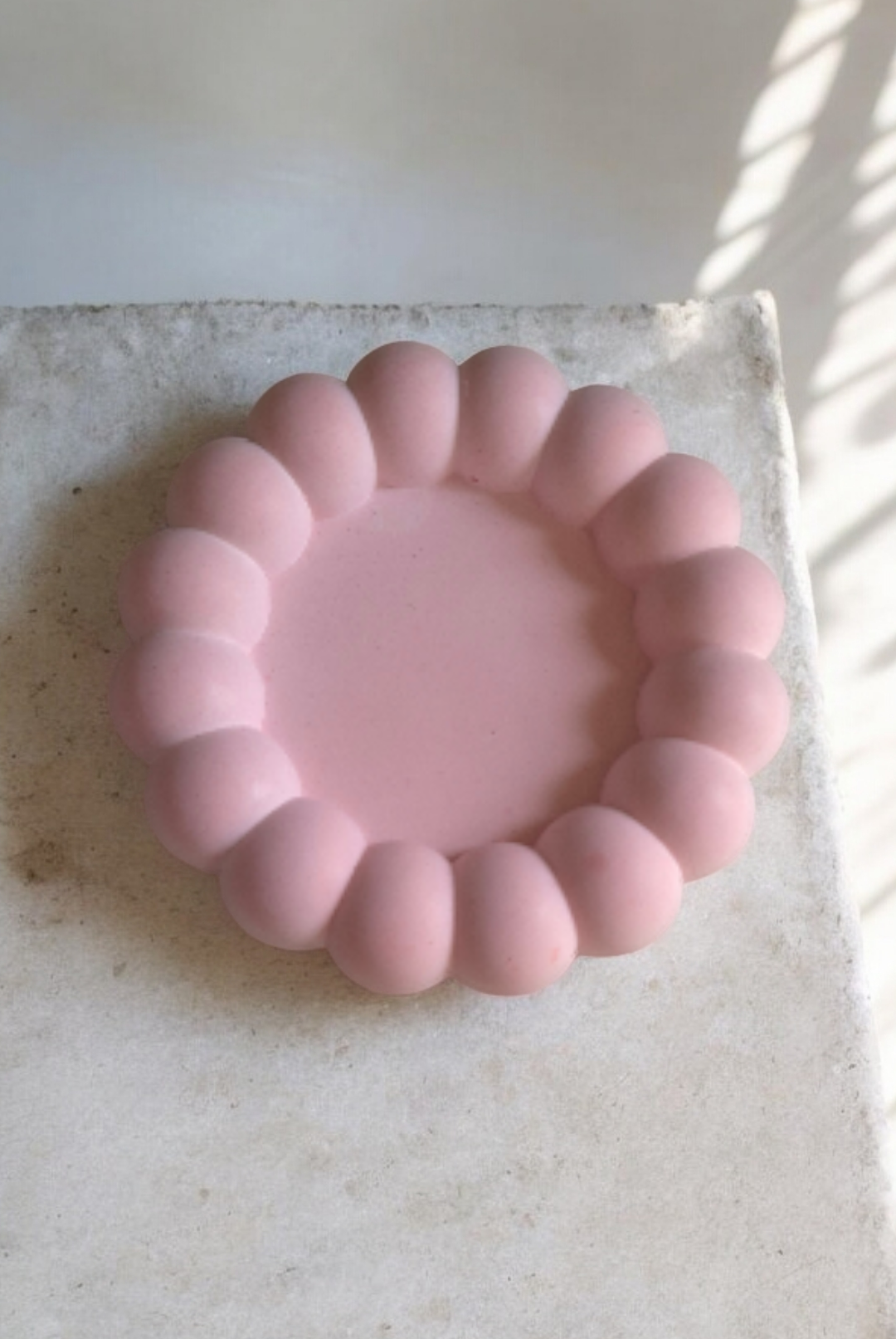 Pink silicone ring on a light stone surface with sunlight casting shadows.