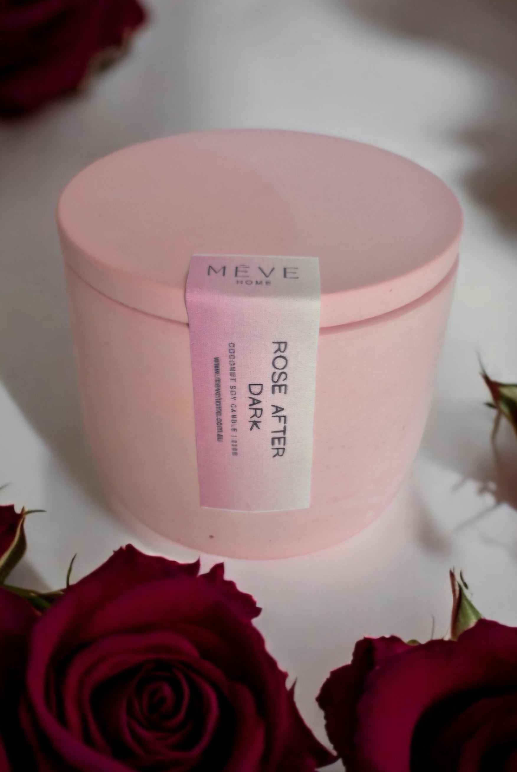 Pink container with a label on a white surface surrounded by red roses