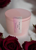 Pink container with a label on a white surface surrounded by red roses